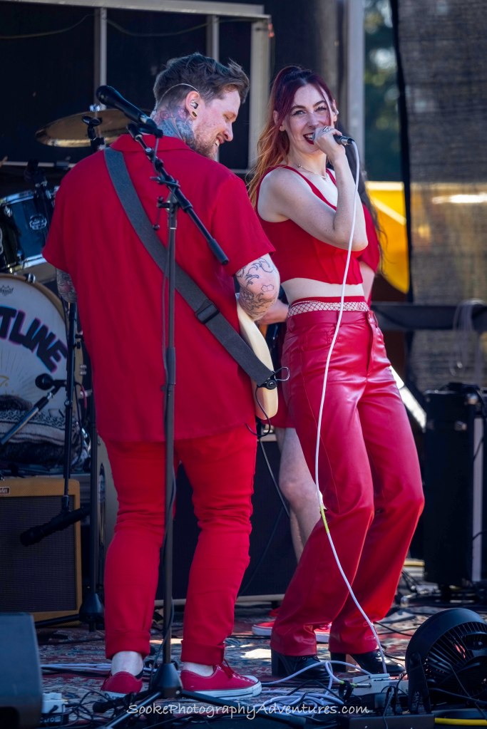 a woman singing and man playing guitar in a band, both wearing red